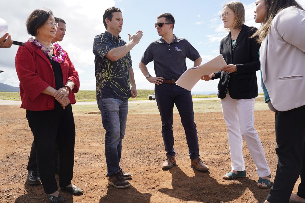Transportation Secretary Pete Buttigieg, center right, listens to Sen. Brian Schatz along the Lahaina Bypass Wednesday, Feb. 21, 2024, in Lahaina. Senator Mazie Hirono, from left, Hawaii Department of Transportation director Ed Sniffen, Federal Highway Administration transportation engineer Lisa Powell and environmental engineer Meesa Otani listen in. (Kevin Fujii/Civil Beat/2024)