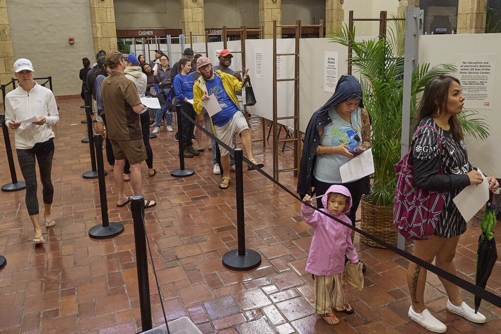 Voters in early voting at Honolulu Hale on King Street in Honolulu were met with torrential downpours as they drove through the election only lane that had been set aside and coned to allow drivers to either hand off their ballots to Poll workers or drop them into several Ballot boxes placed and manned along King Street. (David Croxford/Civil Beat/2024)