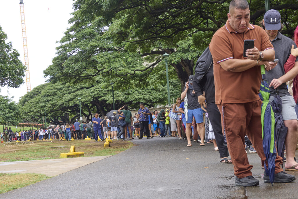 Voters at Honolulu Hale on King Street in Honolulu were met with Poll workers as they drove through the election only lane that had been set aside and coned to allow drivers to either hand off their ballots to Poll workers or drop them into several Ballot boxes placed and manned along King Street.  The lines snaked around the rear of Honolulu Hale, out to the walkway in the rear and then went all the way to Ala Wai and back providing wait times in excess of 2 hours (David Croxford/Civil Beat/2024)