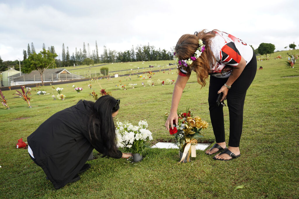 Mae Nani Knight, left, and Lucita Ani-Nihoa place flowers at Theresa Cachuela’s grave Sunday, Dec. 15, 2024, at the Mililani Memorial Park and Mortuary in Mililani. The best friend and mother of Theresa invited Civil Beat to visit her gravesite almost one year after she was killed by her estranged husband Jason Cachuela despite a temporary restraining order. (Kevin Fujii/Civil Beat/2024)