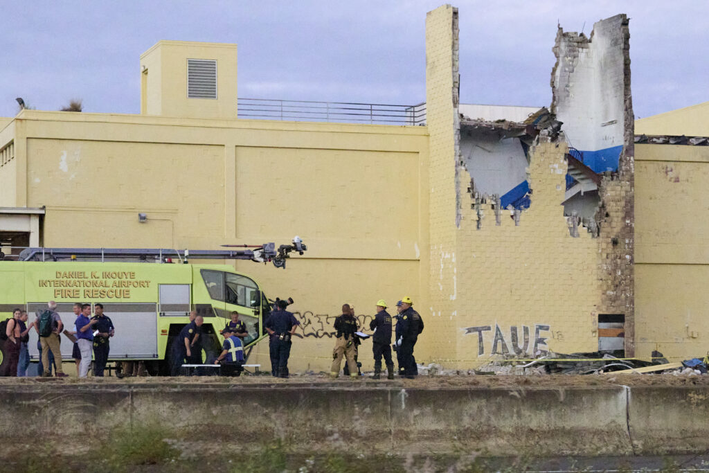 Various Agency Personnel gather at the scene of a Cessna Kamaka Air plane crash in between Aolele Street and at 3129 Ualena Street on Tuesday 12.17.24. Two pilots, believed to be on a training flight, lost control of their aircraft and it turned violently to the left and entered a rapid descent crashing into a state owned building at that address. Emergency personnel were quick to respond but unfortunately neither pilot survived. (David Croxford/Civil Beat/2024)