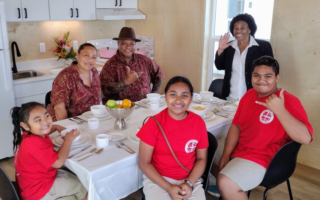 The Folaumoela family, seen here in their new dining room, with FEMA's Evelyn Richardson in the background, was the first family to move in to the FEMA Kilohana Temporary Group Housing in Lahaina. (Léo Azambuja/Civil Beat/2024)